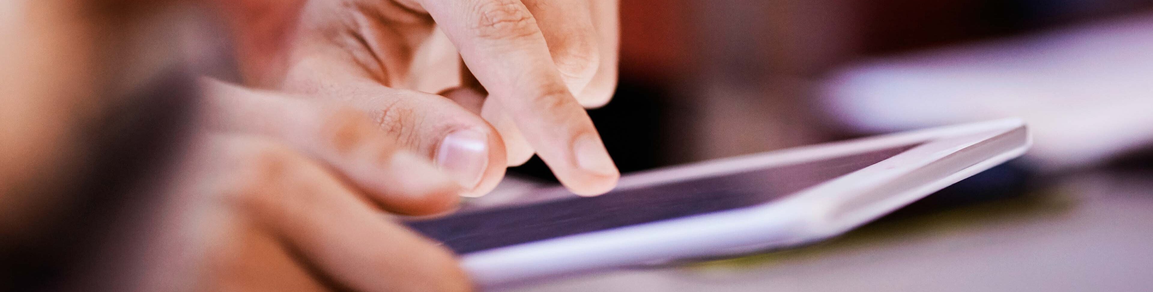 A close-up of a person's hands interacting with a tablet screen, highlighting fingers tapping the device. The background is softly blurred, emphasizing the focus on the hands and the technology.