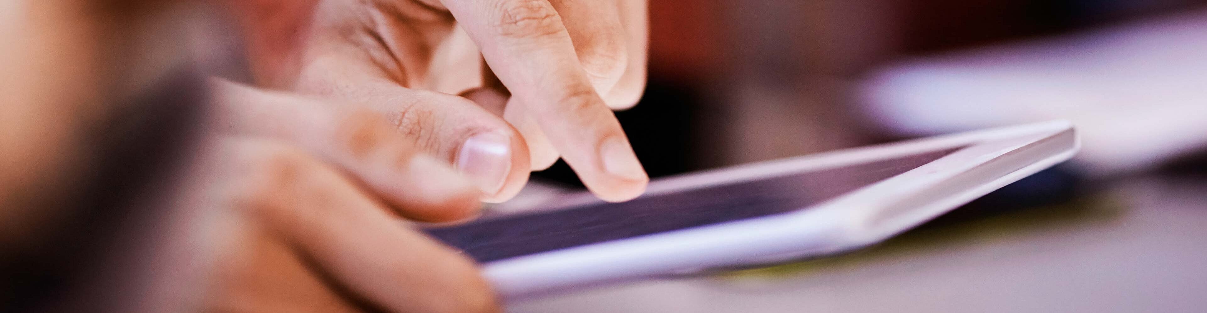 Eine Hand tippt auf einem Tablet. Die Finger sind deutlich zu sehen, während der Bildschirm im Hintergrund leicht erleuchtet ist. Das Bild vermittelt den Eindruck von Aktivität und Interaktion mit digitaler Technologie.