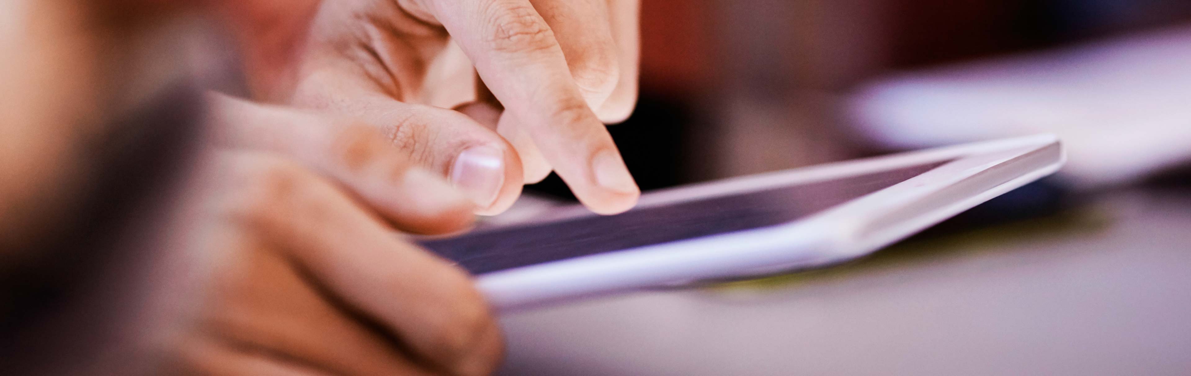 Eine Hand tippt auf einem Tablet. Die Finger sind deutlich zu sehen, während der Bildschirm im Hintergrund leicht erleuchtet ist. Das Bild vermittelt den Eindruck von Aktivität und Interaktion mit digitaler Technologie.