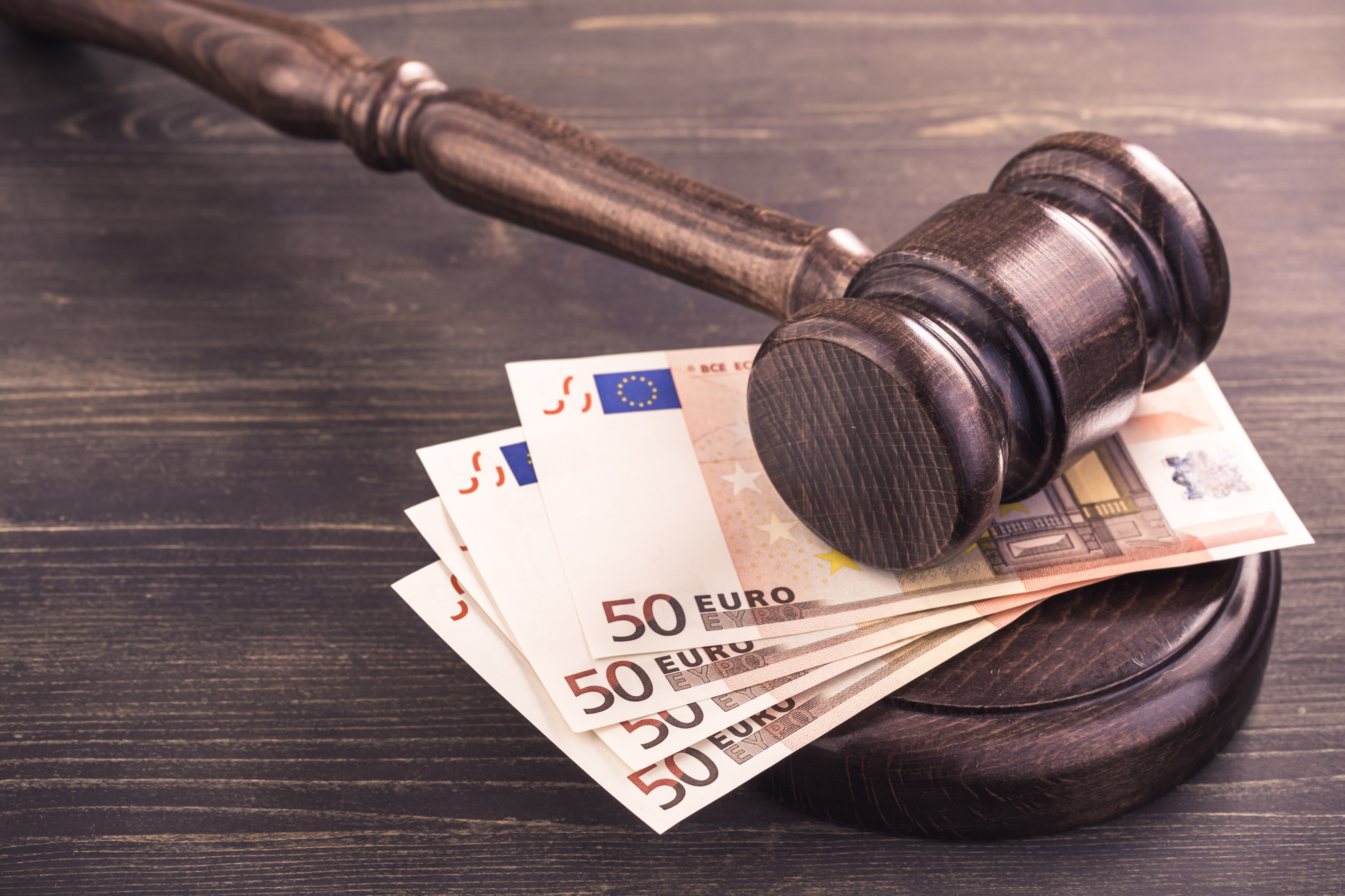 Ein Holzhammer liegt auf mehreren gefalteten 50-Euro-Scheinen. Die Szene symbolisiert rechtliche oder finanzielle Themen, in denen Geld und Gesetze miteinander verbunden sind.
