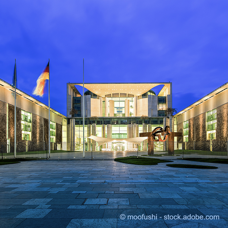 Das Bild zeigt die beeindruckende Fassade des Bundeskanzleramts in Berlin bei Nacht. Der moderne Gebäudekomplex ist von einem klaren, dunklen Himmel umgeben und wird von stilvollen Beleuchtungselementen erhellt. Vor dem Gebäude sind Skulpturen und eine gepflegte Grünfläche sichtbar.