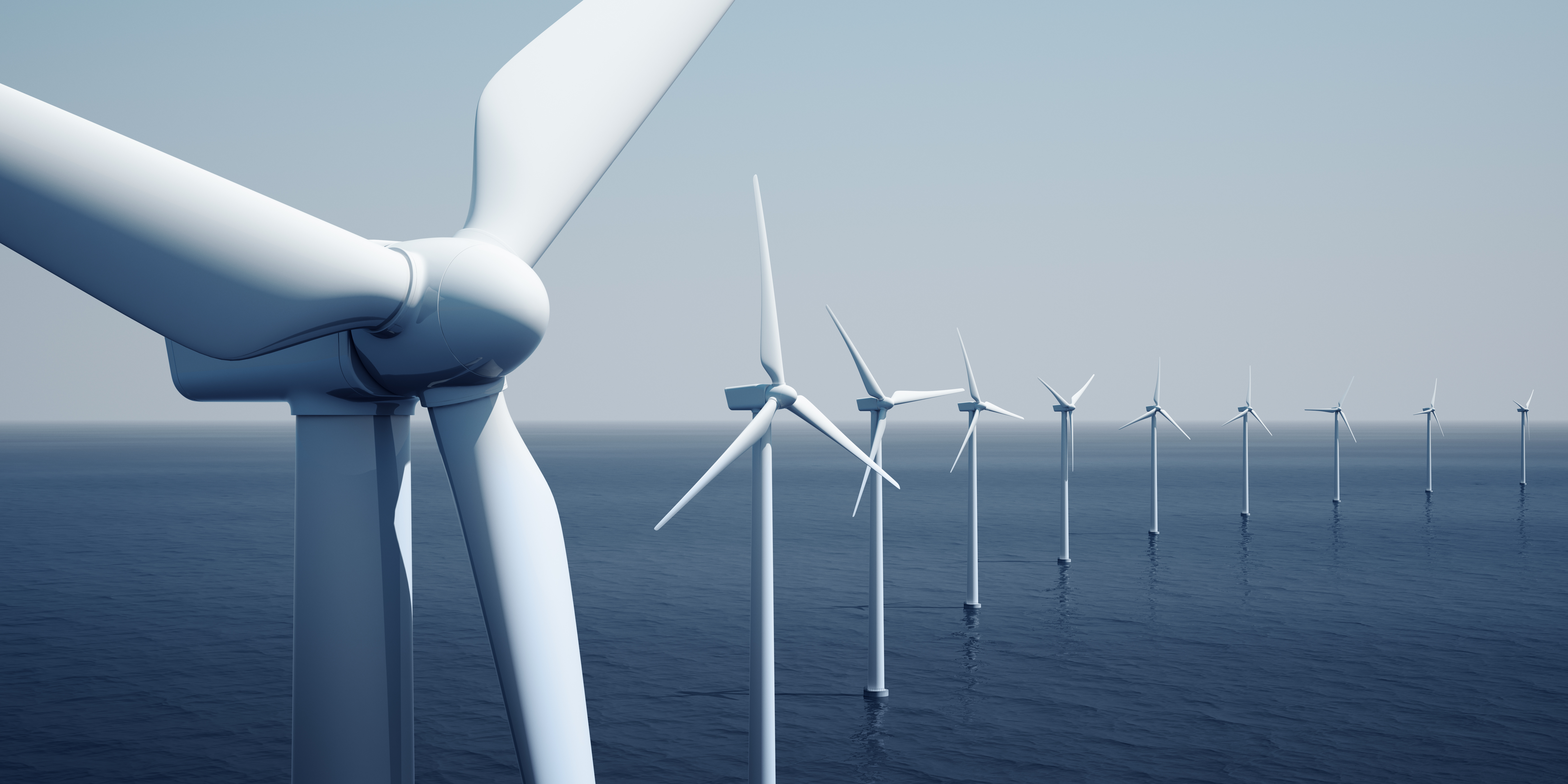 Windkraftanlagen sind in einer Reihe im Meer aufgestellt. Die Turbinen sind hoch und weiß, mit langen Rotorblättern, die sich im Wind drehen. Die Umgebung ist ruhig und blau, mit Wasser, das sich bis zum Horizont erstreckt.