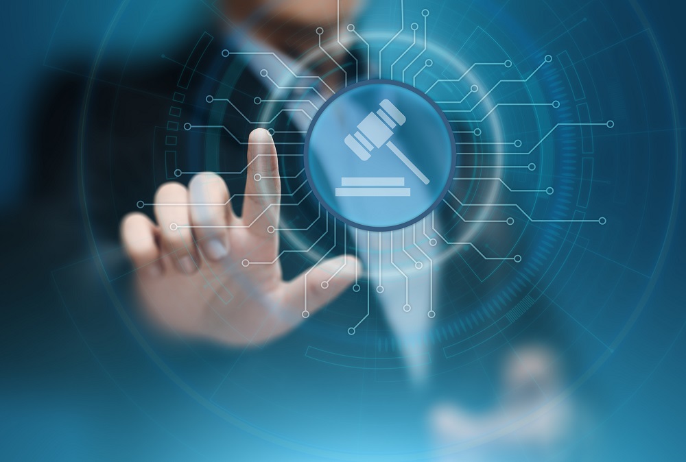A person in a suit reaches toward a digital icon depicting a gavel and legal scales, set against a blue, technology-themed background. The image symbolizes the intersection of law and technology.