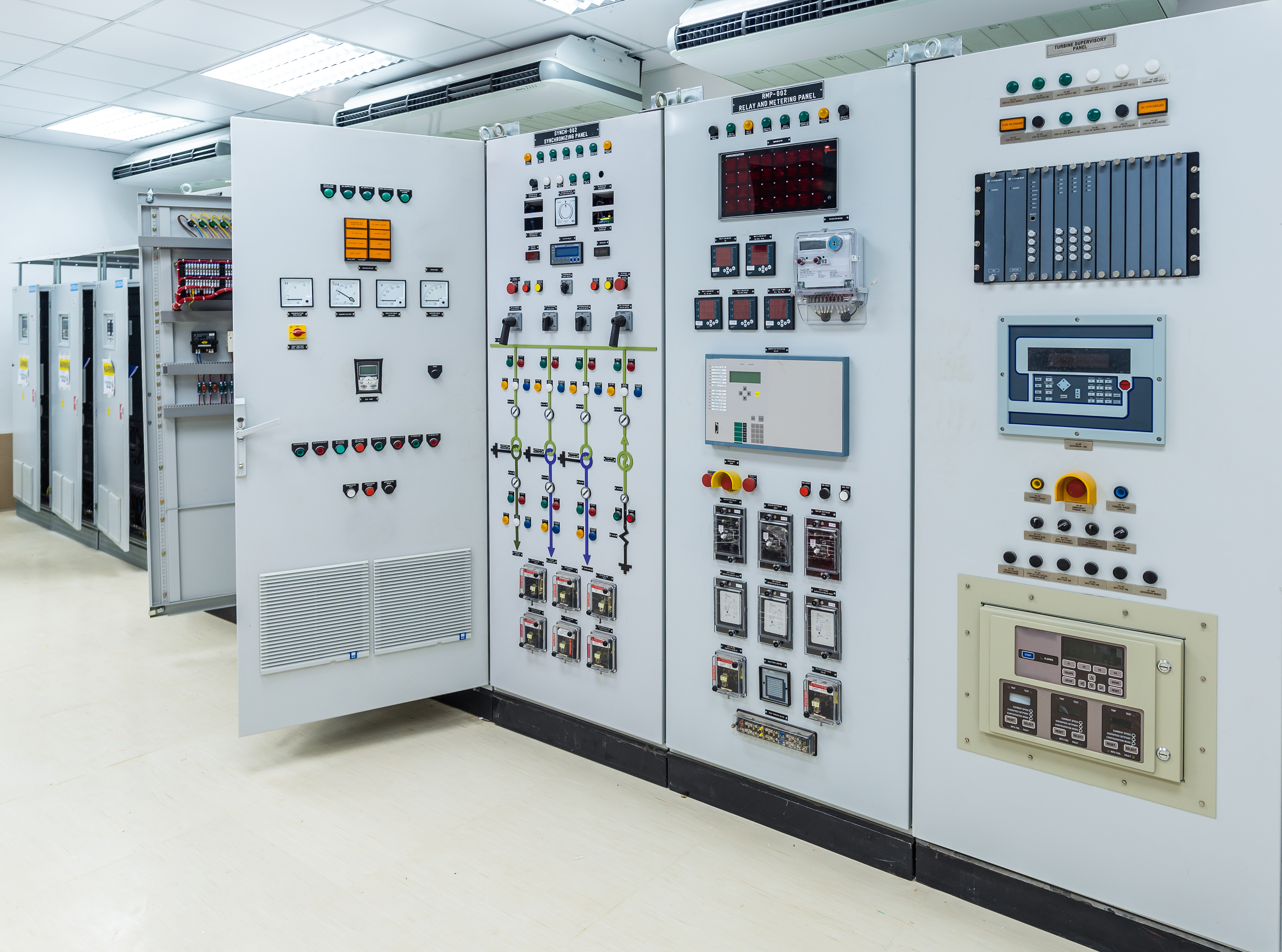 A control room featuring multiple electrical panels. Each panel is equipped with various buttons, switches, gauges, and digital screens used for monitoring and controlling electrical systems. The environment is well-lit and organized, reflecting a technical workspace focused on operational efficiency.