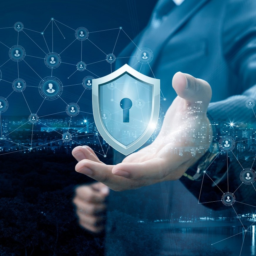 Eine Hand hält ein digitales Schild mit einem Schloss-Symbol, das Sicherheit darstellt. Im Hintergrund sind Netzwerke und Icons von Personen abgebildet, die auf digitale Verbindungen hinweisen. Die Szene vermittelt das Thema Cyber-Sicherheit und den Schutz von Informationen.