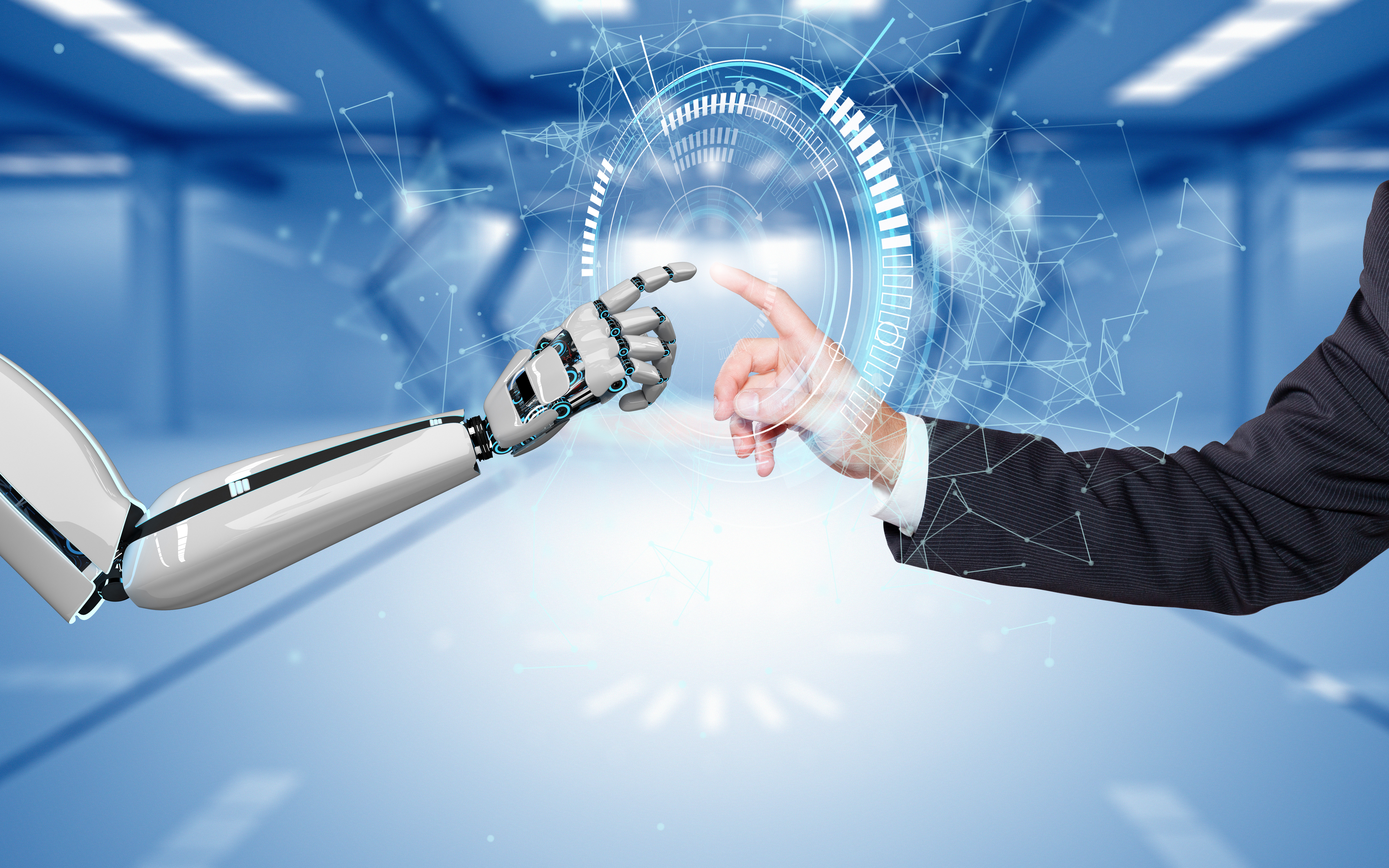 Ein humanoider Roboterarm greift mit einem Finger nach der Hand eines Menschen, der einen Anzug trägt. Zwischen den Händen sind digitale Elemente sichtbar, die Interaktion und Technologie symbolisieren. Der Hintergrund ist unscharf und vermittelt ein futuristisches Ambiente.