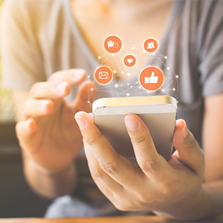 Eine Person hält ein Smartphone in den Händen. Über dem Gerät schweben verschiedene Icons, die Kommunikation, soziale Interaktionen und Likes symbolisieren. Das Bild vermittelt den Eindruck digitaler Vernetzung und Interaktion.