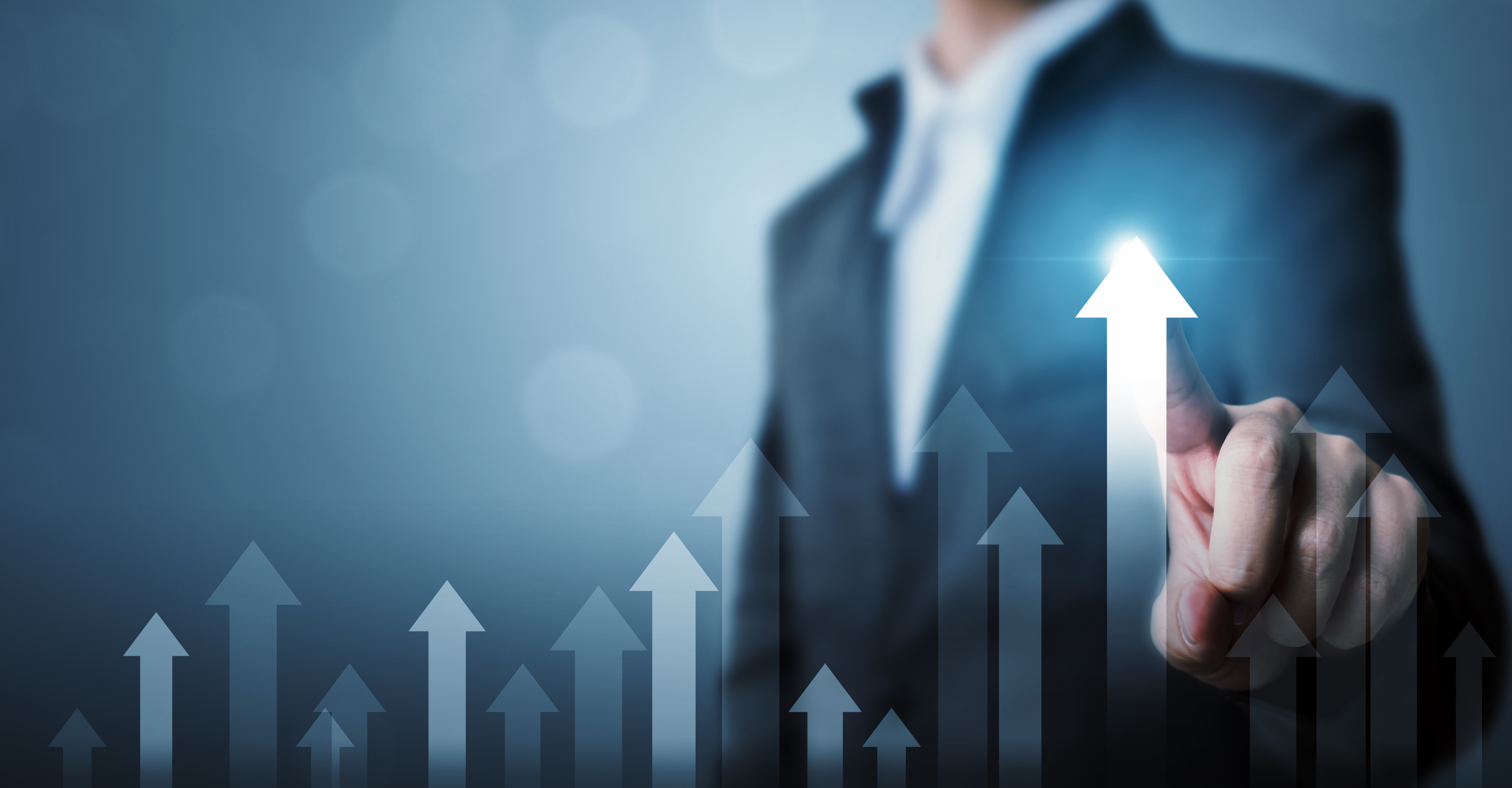 A person in a suit points upward, signaling growth or progress. Behind them, various upward-pointing arrows illustrate a positive trend. The overall tone suggests success and forward movement, emphasizing advancement or improvement in a professional context.