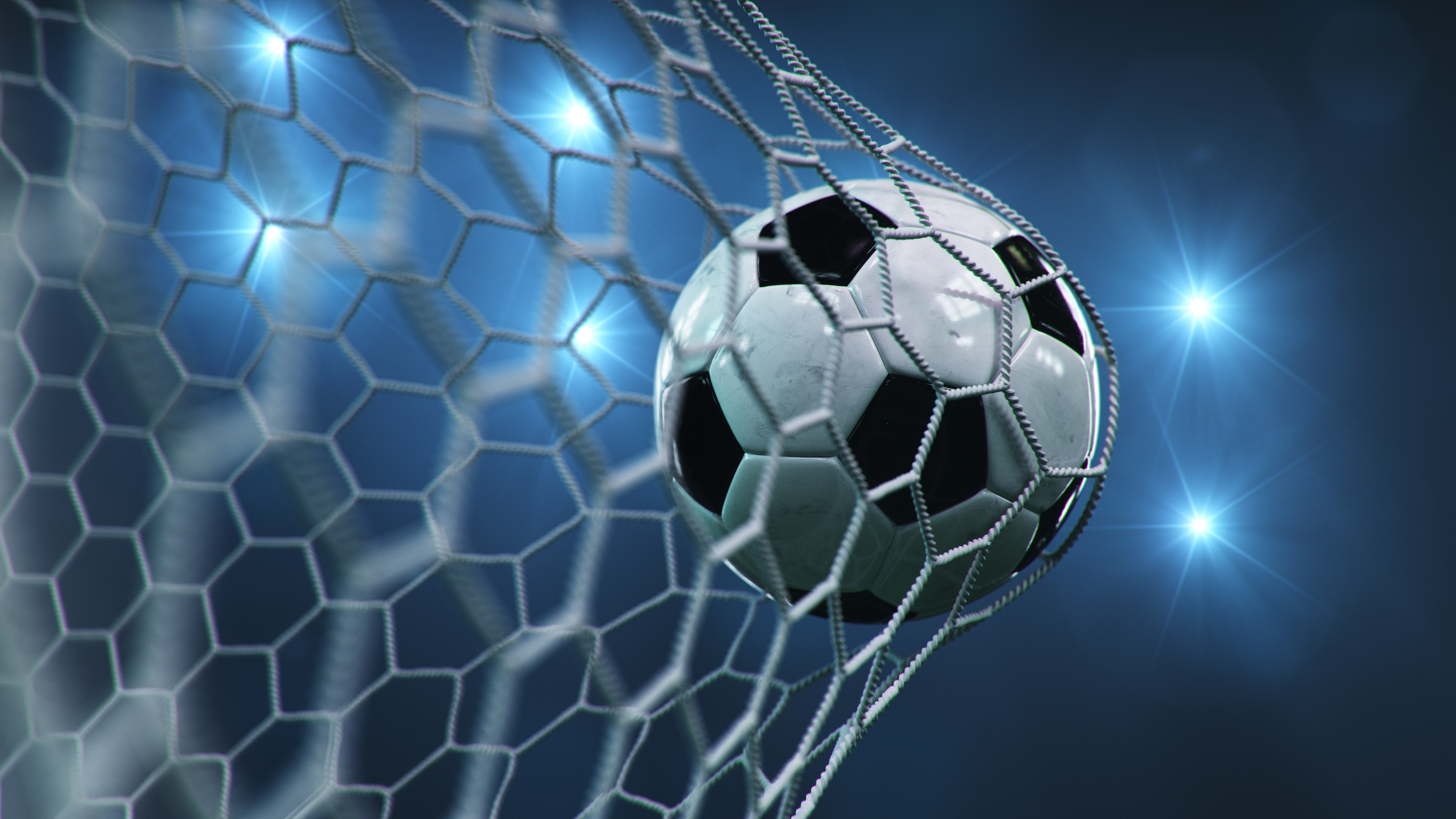 Ein Fußball fliegt ins Netz eines Tores. Das Netz ist deutlich zu sehen, und im Hintergrund sind mehrere Lichtquellen, die eine sportliche Atmosphäre erzeugen. Der Fokus liegt auf dem Ball und dem Netz, was den Moment eines Tores symbolisiert.