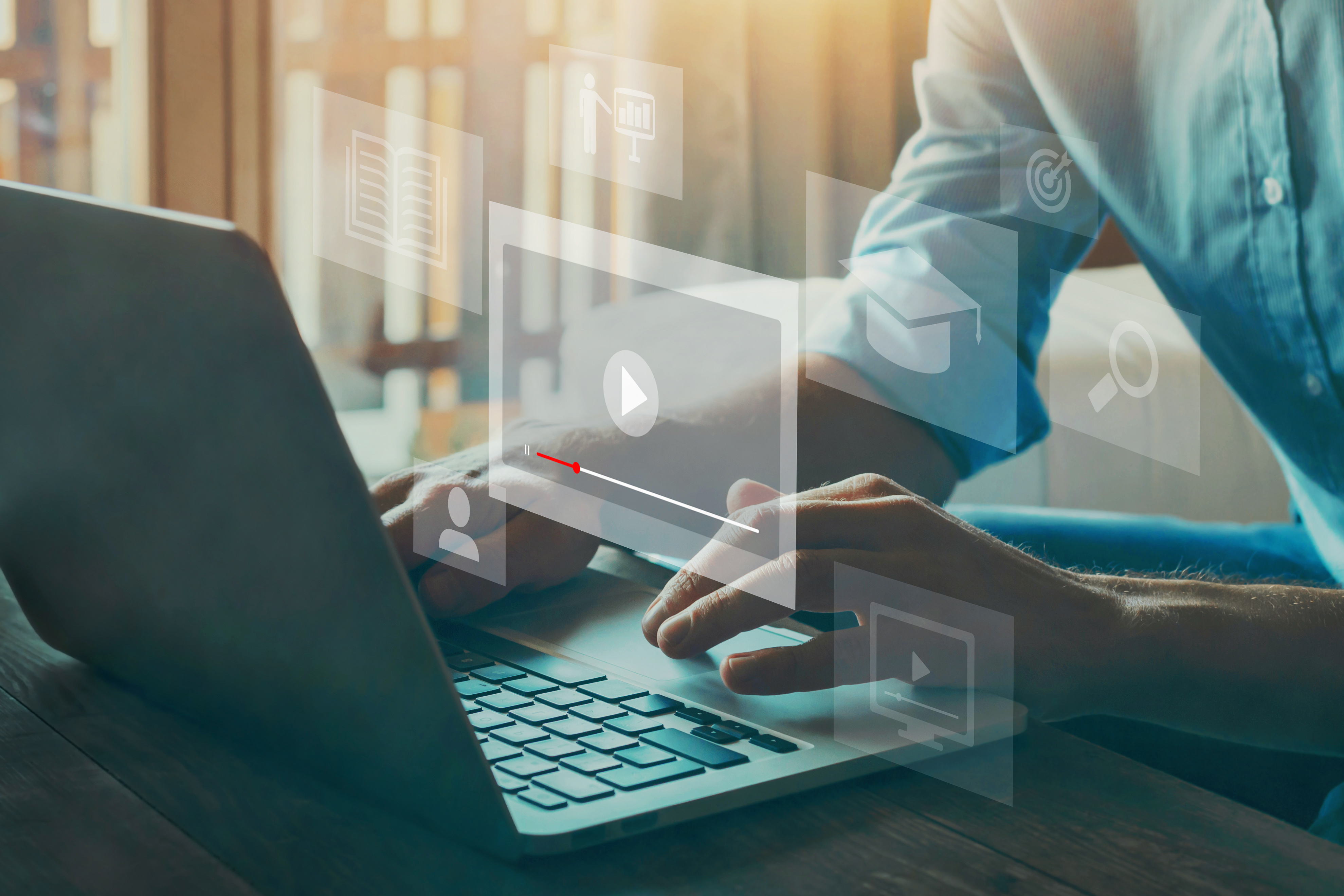 Ein Mann nutzt einen Laptop, während digitale Symbole wie ein Videoplayer, ein Buch und eine Grafik darauf projiziert werden. Das Bild vermittelt den Eindruck von digitalen Lern- oder Arbeitsaktivitäten in einer modernen Umgebung mit natürlichem Licht.