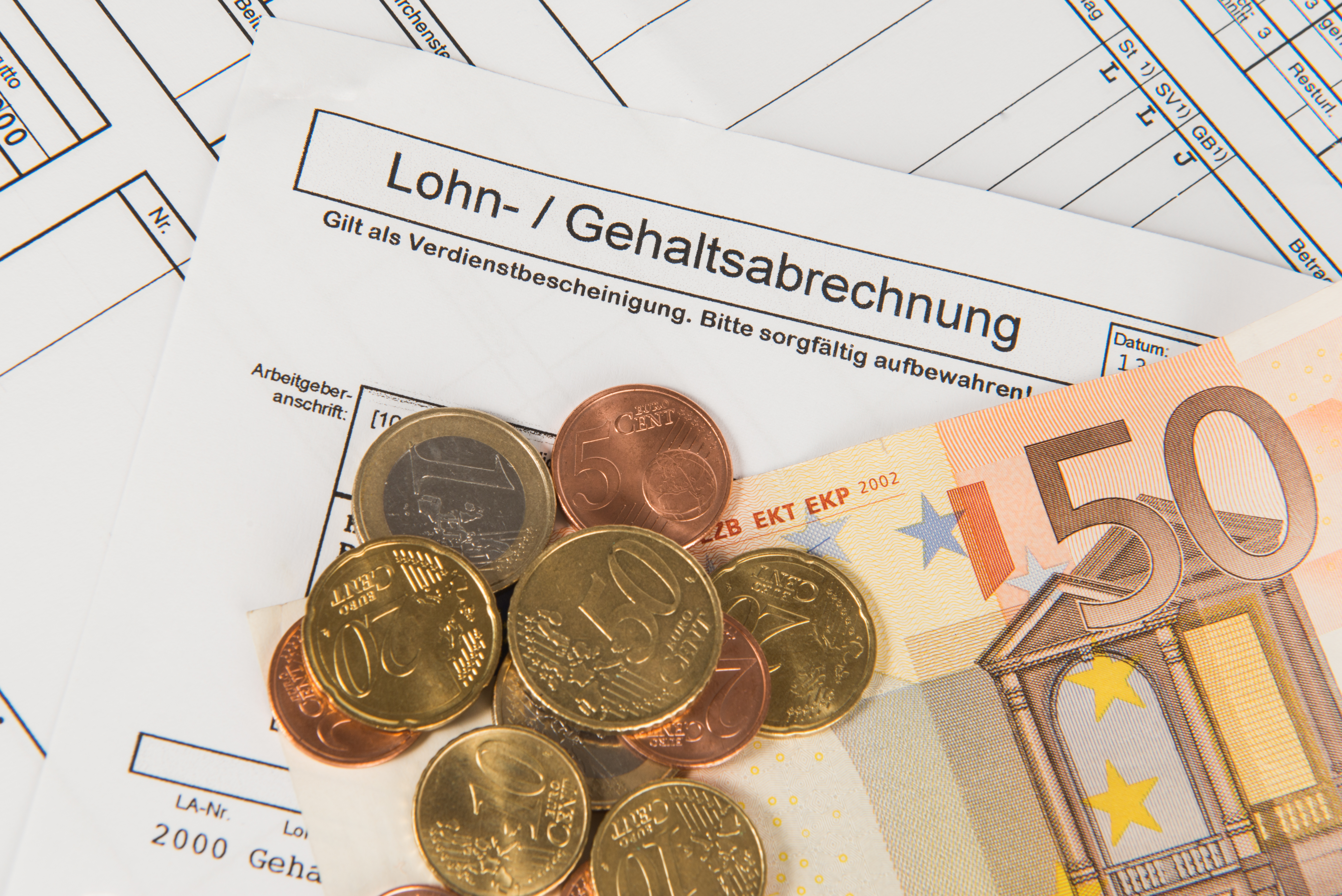 Auf einem Lohn- und Gehaltsabrechnungsformular liegen mehrere Euro-Münzen und ein 50-Euro-Schein. Das Formular enthält wichtige Informationen zur Verdienstdokumentation. Es ist wichtig, diese Unterlagen sorgfältig aufzubewahren.