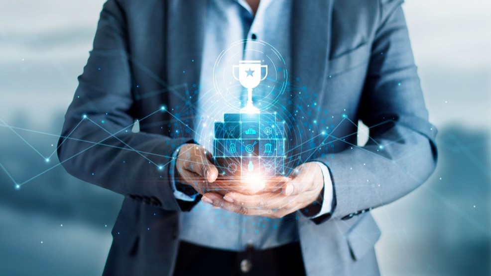 Ein Mann in einem Anzug hält eine leuchtende, digitale Trophäe über einem stilisierten Podest. Um ihn herum sind grafische Symbole, die Erfolge und Dienstleistungen darstellen. Das Bild vermittelt den Eindruck von Innovation und Erfolg im digitalen Bereich.
