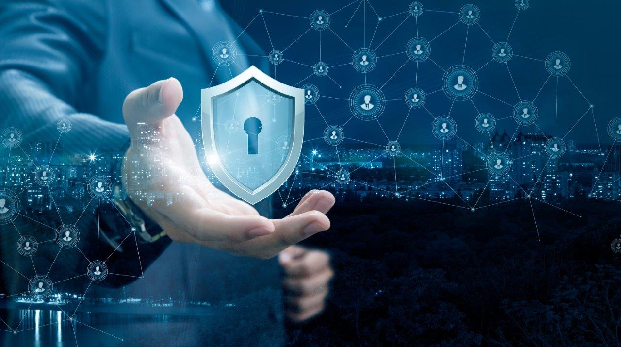 Eine Hand hält ein transparentes Schild mit einem Schloss-Symbol. Im Hintergrund ist ein Netzwerk von Benutzer-Icons und Datenpunkten sichtbar, das digitale Sicherheit und Vernetzung symbolisiert. Die Farbgebung ist dunkelblau mit Lichtakzenten, was eine moderne, technologische Atmosphäre schafft.