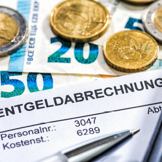 Eine Rechnung für Entgeltabrechnung liegt auf einem Tisch, umgeben von Euro-Scheinen und Münzen. Die Dokumente zeigen Personal- und Kostenummern. Ein Kugelschreiber liegt ebenfalls neben den Unterlagen.