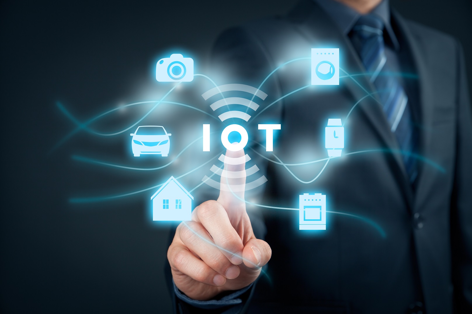 Ein Geschäftsmann berührt mit einem Finger das Wort „IoT“, umgeben von symbolhaften Darstellungen von Geräten wie Kamera, Auto, Haus und Smartwatch, die die Vernetzung im Internet der Dinge darstellen.
