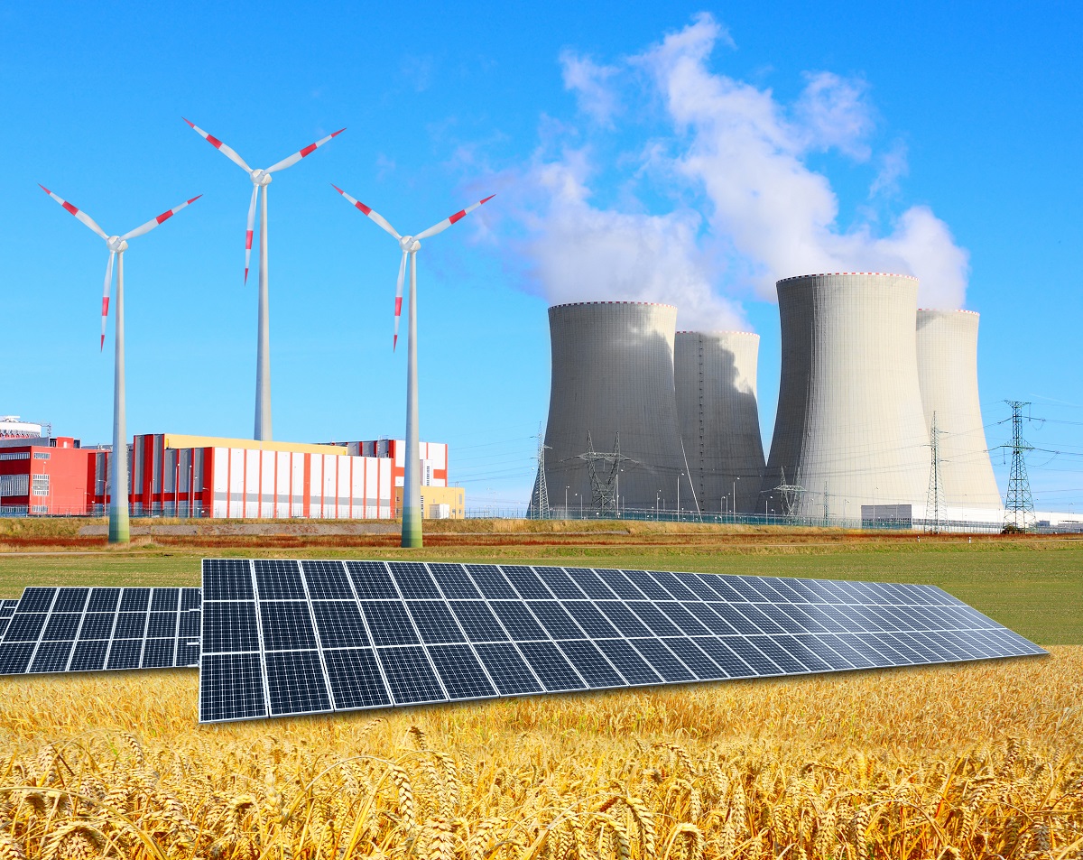 Das Bild zeigt eine Landschaft mit Windkraftanlagen im Hintergrund und einem Photovoltaikfeld im Vordergrund. Im Hintergrund sind Kühltürme eines Kraftwerks sichtbar. Diese Elemente verdeutlichen das Thema erneuerbare Energie und verschiedene Energiequellen.
