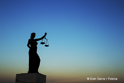 A silhouette of a figure representing justice stands holding scales, set against a gradient sky transitioning from blue to orange. The image symbolizes fairness and the legal system.