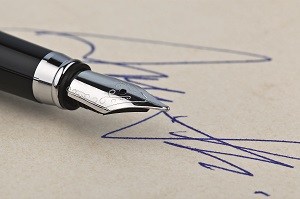 Ein schwarzer Füllfederhalter liegt auf beige-farbenem Papier. Neben der Feder sind blaue Unterschriften oder Kritzeleien sichtbar. Die Füllfeder hat silberne Details und ist scharf fokussiert.