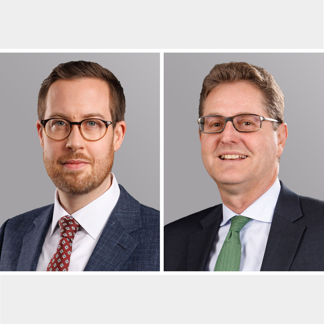 Two professional headshots side by side. The left image features a man with medium-length brown hair and a beard, wearing glasses and a blue suit with a white shirt and patterned tie. The right image shows a man with short brown hair, wearing glasses, a dark suit, and a light blue shirt with a green tie.