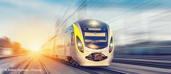A high-speed train moves swiftly down the tracks, with a bright sunrise in the background. The image conveys a sense of motion and energy, highlighting the train's sleek design and modern features.