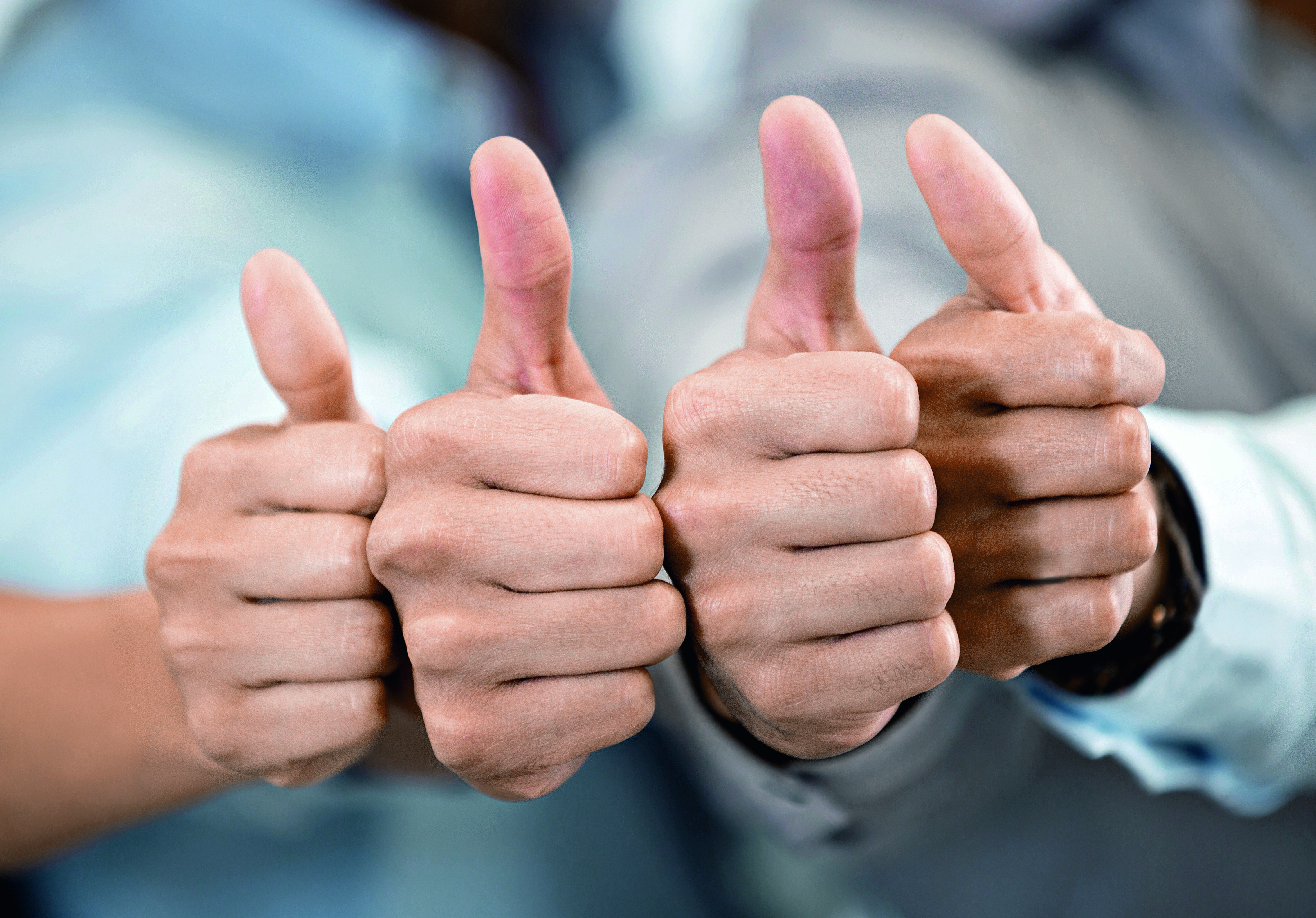 Four hands with raised thumbs are shown, indicating approval or a positive gesture. The hands belong to indistinct individuals, demonstrating unity and agreement. The focus is on the thumbs, symbolizing encouragement and support.