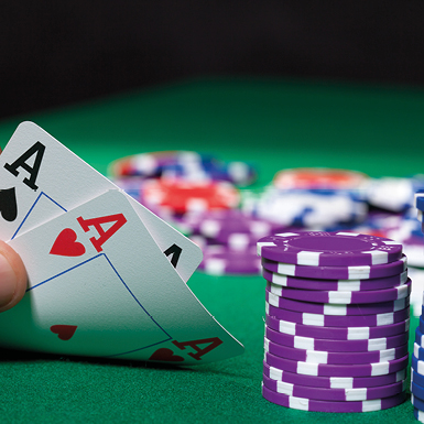 Ein Spieler hält zwei Karten mit Assen in der Hand, während ein Stapel von lila Spielchips daneben liegt. Der Hintergrund zeigt einen grünen Spieltisch.