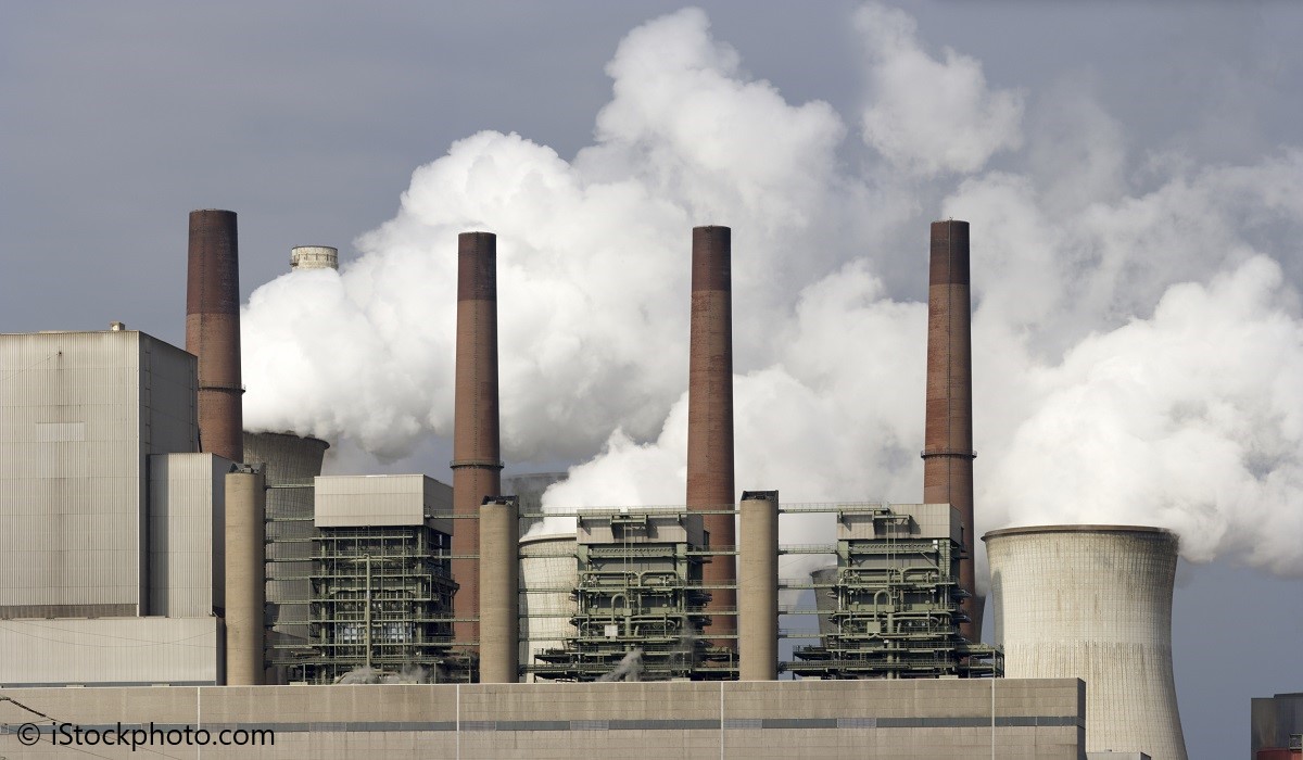 Ein Kraftwerk mit mehreren hohen Chimneys stößt dichten Rauch und Dampf aus. Die Anlage ist groß und industriell gestaltet, umgeben von einem bedeckten Himmel. Die Emissionen sind deutlich sichtbar, was auf einen aktiven Betrieb hinweist.