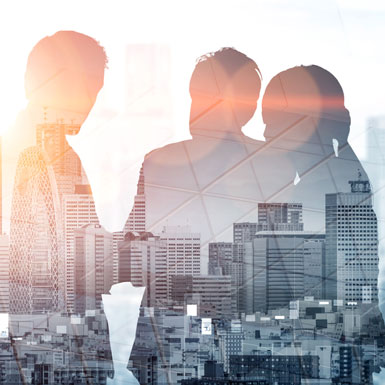 Silhouettes of three people are engaged in conversation against a backdrop of a city skyline. The image conveys a sense of collaboration and urban life, with buildings and a hazy overlay creating a modern, dynamic atmosphere.
