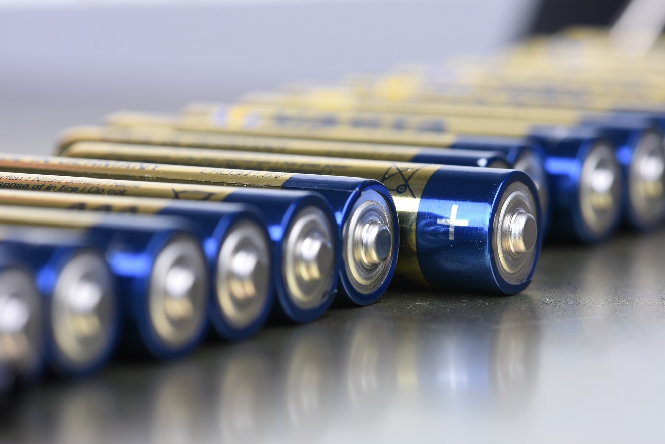 Eine Reihe von Batterien mit blauer Ummantelung, die gleichmäßig nebeneinander angeordnet sind. Die Plus-Pol-Seiten der Batterien sind sichtbar, während die Rückseiten nicht sichtbar sind. Die Batterien haben goldene Schriftzüge, die teilweise lesbar sind.