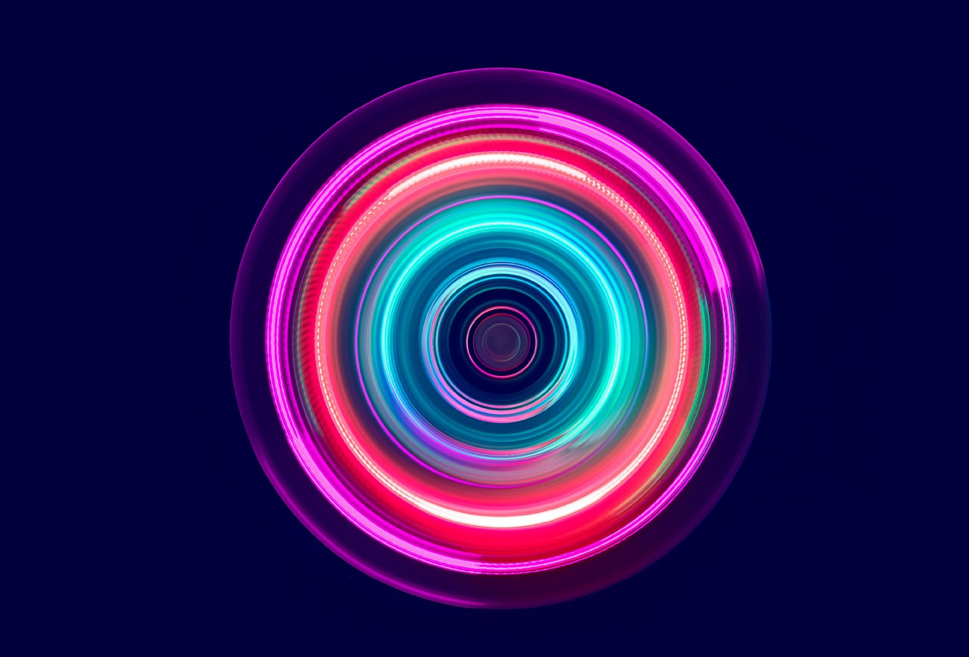 A circular pattern of vibrant, glowing colors in shades of pink, blue, and green radiates from the center, creating an impression of movement and energy against a dark background. The design emphasizes concentric circles, evoking a sense of dynamism and light.