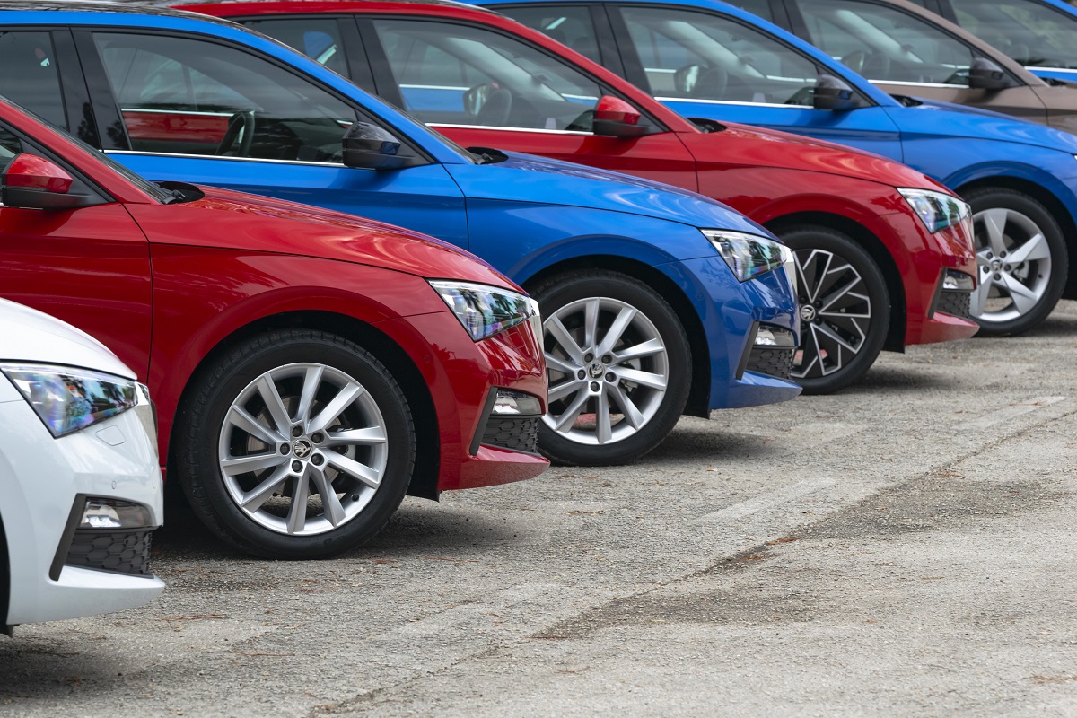 Es sind mehrere Pkw in verschiedenen Farben in einer Reihe geparkt. Die Autos sind hauptsächlich rot, blau und weiß, mit gut sichtbaren Felgen. Der Fokus liegt auf der Seitenansicht der Fahrzeuge, die auf einem asphaltierten Parkplatz stehen.