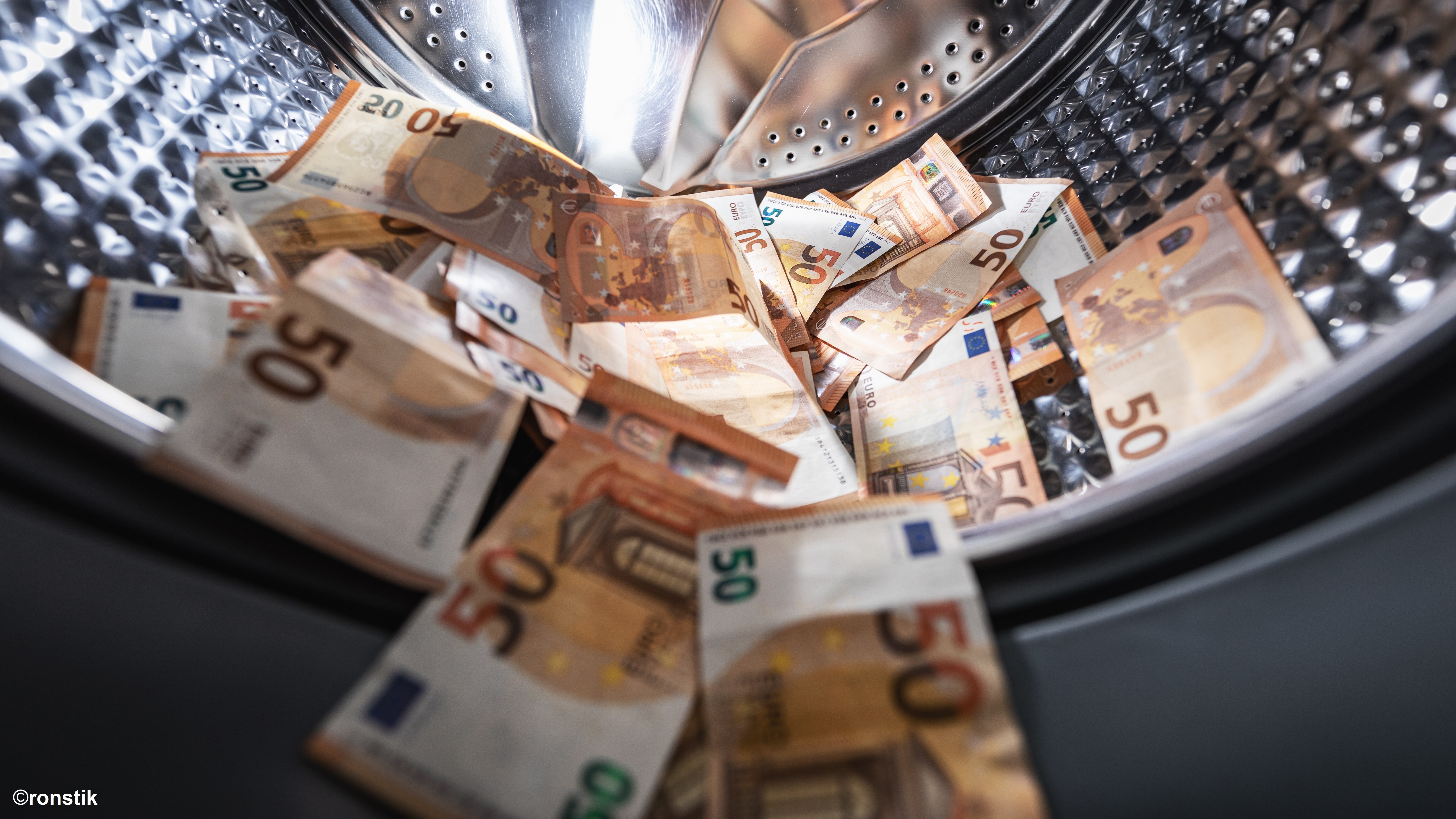 Ein Blick in eine Waschmaschine, die mit mehreren 50-Euro-Scheinen gefüllt ist. Die Geldscheine liegen übereinander und sind teilweise sichtbar, was den Eindruck von Unordnung und ungewöhnlichem Inhalt vermittelt.