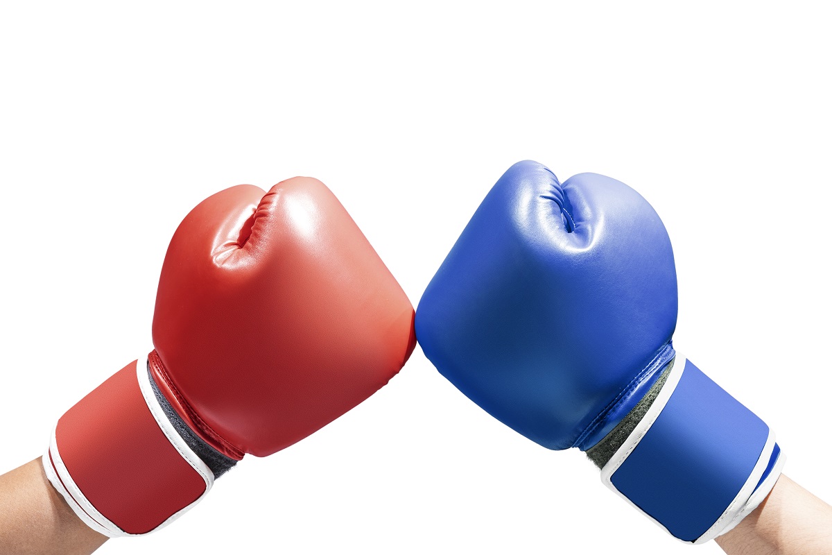 Two boxing gloves, one red and one blue, are colliding in the center of the image. The gloves are depicted in a dynamic pose, symbolizing competition or a sporting challenge. The background is plain, emphasizing the gloves.