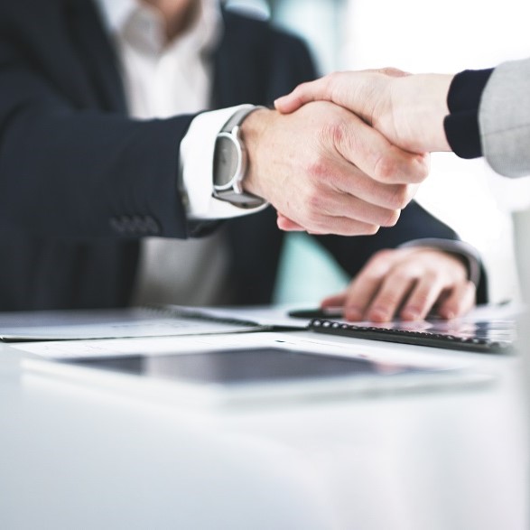 Two people are shaking hands over a table. The focus is on their hands as they engage in a professional agreement. The setting appears to be an office, suggesting a business meeting or negotiation.