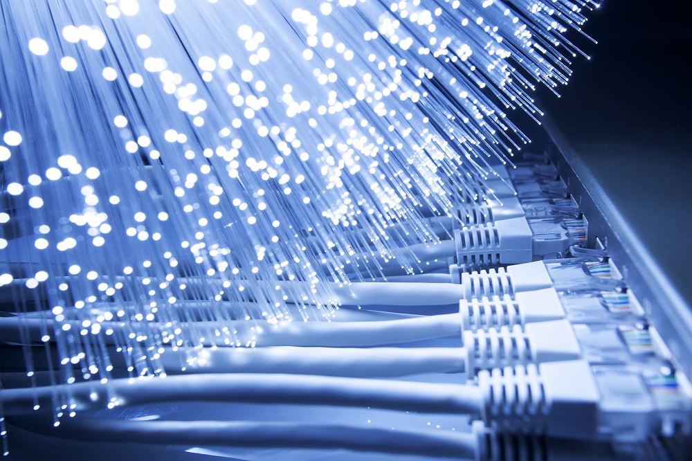 Ein Näheblick auf eine Vielzahl von Glasfaserkabeln mit leuchtenden Lichtpunkten. Im Vordergrund sind mehrere Ethernet-Kabel sichtbar, die geordnet nebeneinander angeordnet sind. Die Gesamtstimmung vermittelt eine moderne Technologie-Umgebung.
