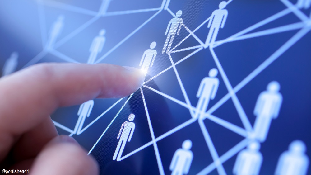 Ein Finger berührt einen Bildschirm, der ein Netzwerk von stilisierten Personen zeigt, die durch Linien verbunden sind. Das Bild symbolisiert Interaktion oder Vernetzung in einem digitalen Kontext.