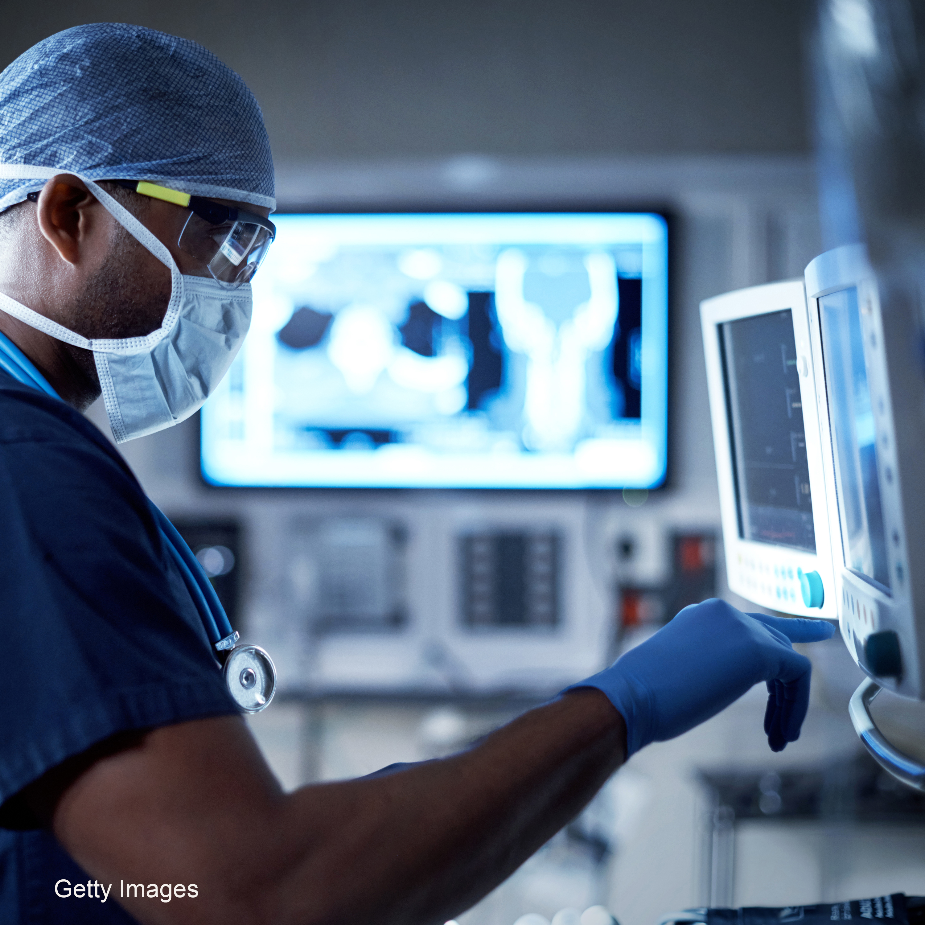 Ein Mediziner in Schutzkleidung bedient ein medizinisches Gerät in einem Krankenhaus. Im Hintergrund ist ein Bildschirm mit medizinischen Untersuchungsbildern zu sehen. Die Szene vermittelt eine Atmosphäre von Präzision und Professionalität in der Patientenversorgung.