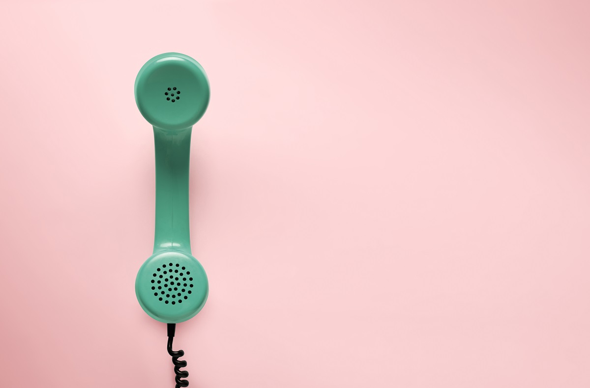 Ein mintgrüner Telefonhörer hängt an einer schwarzen Spirale. Der Hintergrund ist rosa. Der Hörer zeigt die typischen Löcher für Lautsprecher und Mikrofon.