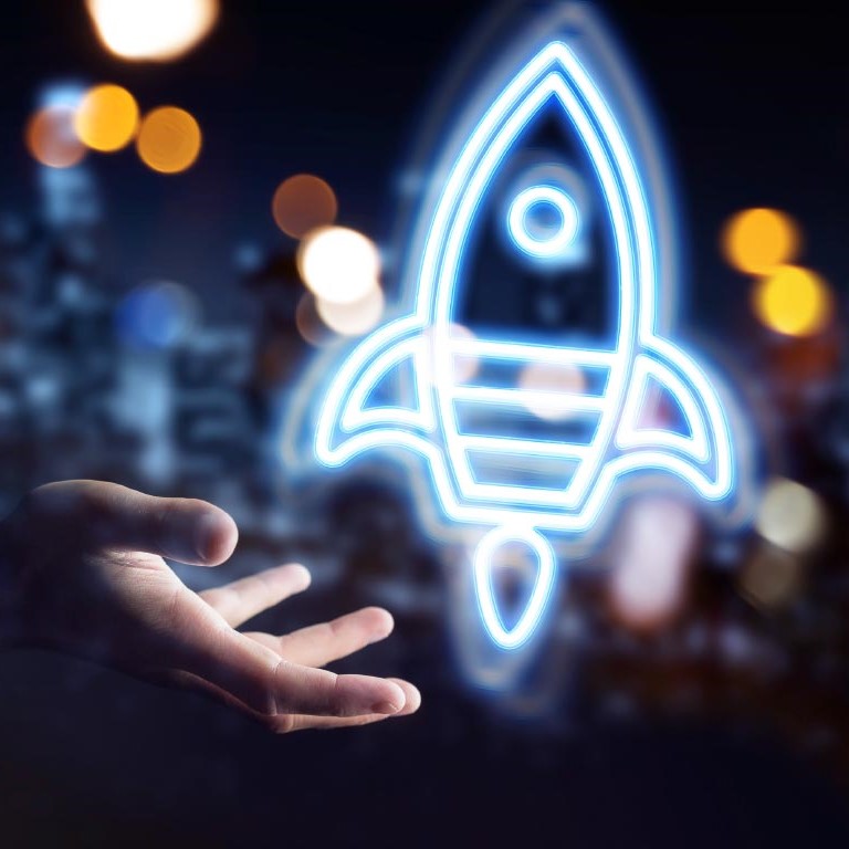 Eine Hand hält sich offen, während über ihr eine leuchtende, neonblaue Rakete schwebt. Der Hintergrund ist unscharf mit warmen, verschwommenen Lichtern, die eine dynamische Atmosphäre schaffen.
